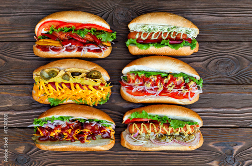 Fotomural A lot of big delicious hot dogs with sauce and vegetables on wooden background