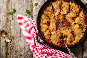 Wall Mural - Cherry Cobbler with cinnamon and chocolate on a rough wooden board with cloth and leaves of cherry 