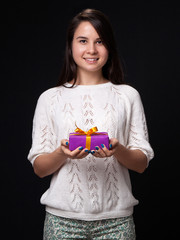 Young woman holding a present in the hands, black background