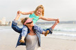 © GeoffGoldswain - Young girl sitting on mom's shoulder while walking on beachfront