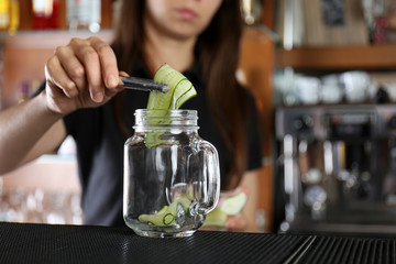 Poster - Woman hands putting cucumber into glass jar on bar counter