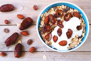 Top view of a healthy bowl of Muesli with whole grain, oats, dried fruit, nuts and date fruit with yogurt on a wooden table.