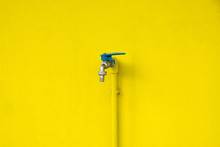 Closeup Faucet On Concrete Yellow Wall Background. Water Leaking