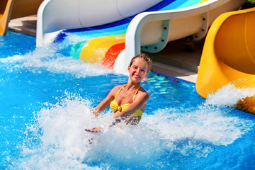 Wall Mural - Child on water slide at water park . Child girl in water splashes.