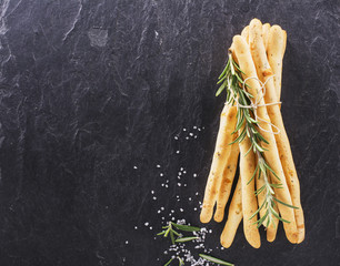 Bread sticks with salt and herbs on dark board, from overhead.