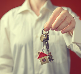 woman is handing a house key. Key with a keychain in the shape o