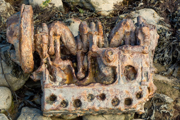 Corroded engine rusting on rocky coast. Abandoned motor red and eroded with rust lying amonst stones and seaweed below high tide mark on the shore