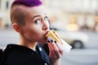 © raisondtre - Charming young girl with short purple hair eats a hot dog on the street on the way to the office.