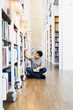 © Astrakan Images - Man sitting on floor in library, choosing books