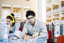 Portrait Of Confident Young Man Writing Notes While Sitting In Library