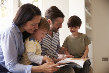 Family Sitting On Window Seat Reading Story At Home Together