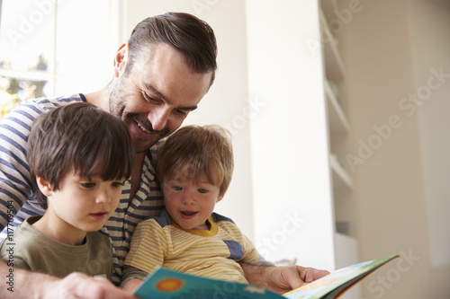 Fotografie, Obraz Close Up Of Father And Sons Reading Story At Home Together