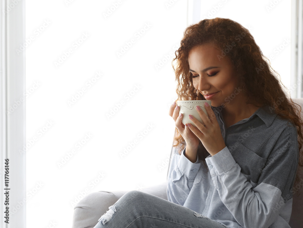Beautiful African American girl drinking coffee on couch