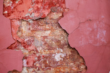 Flaking Plaster On The Brick Wall Of An Ancient Building. Old Wall Texture. Peeling Maroon Paint, Plaster And Exposed Brick Wall. 