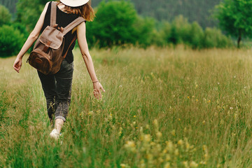 stylish hipster woman walking in grass and holding  in hand herb