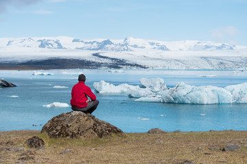 Wall Mural - Tourist in a red jacket sits on the shores of the glacial lagoon