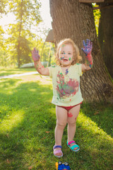 Two-year old girl stained in colors against green lawn