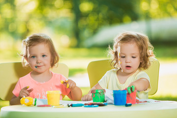 Two-year old girls painting with poster paintings together against green lawn