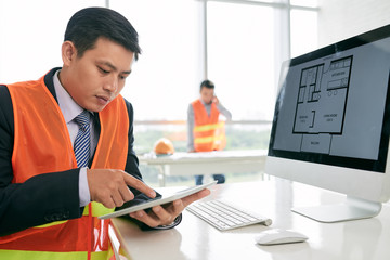 Wall Mural - Asian engineer examining blueprint in his digital tablet