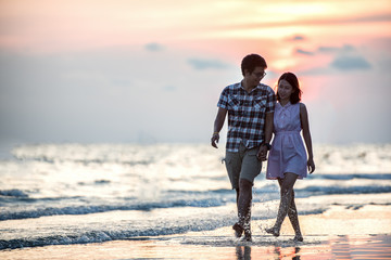 Wall Mural - Couple walking on beach. Young happy interracial couple walking on beach smiling holding around each other