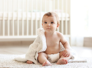 cute baby sitting beside his bed on the floor