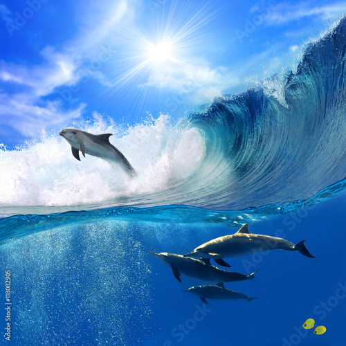 Obrazy Delfiny oceanview-with-sunlight-a-flock-of-playful-dolphins-swimming-underwater-and-one-of-them-leaping-out-from-big-sea-surfing-wave