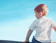© guas - Little child boy sitting pensive looking away outdoors over blue