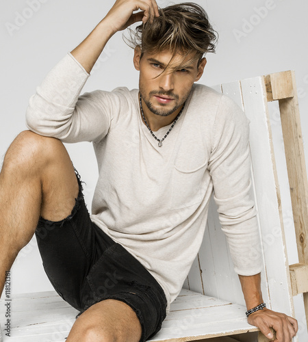 Cuadros en Lienzo Portrait of handsome man with hand in his hair and sitting on pa