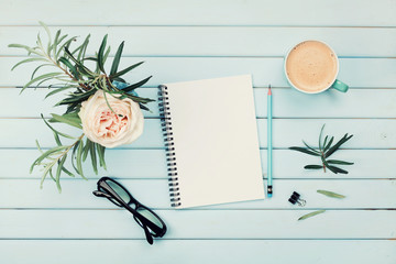 Wall Mural - Morning coffee cup, clean notebook, pencil, eyeglasses and vintage rose flower in vase on blue rustic table top view. Planning and design concept. Cozy breakfast. Flat lay styling.