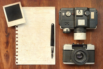 blank paper with pen, photo frames and camera on wooden background with sunlight vintage color