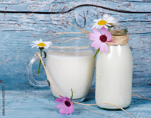Fotografie, Obraz Tasty and healthy: fresh milk in bottle and glass with flowers in front of old,
