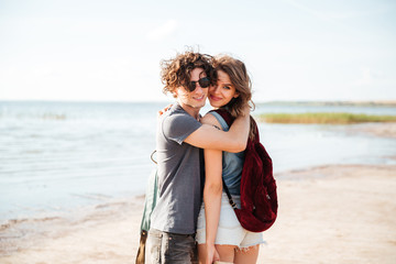 Poster - Couple with backpacks standing and hugging on the beach