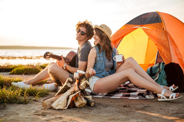 couple sitting near campfire and playing guitar