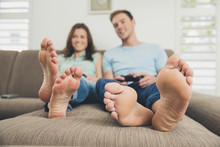 Couple Barefoot On Sofa Using Video Game Controller