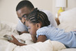 © Hello Lovely/Blend Images - African American father and daughter using digital tablet on bed