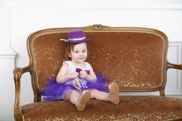 beautiful little girl in purple skirt and hat sitting on couch