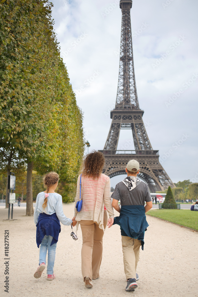 Mother, son and daughter walk in the park near the Eiffel Tower in Paris, view from the back - obrazy, fototapety, plakaty 