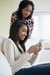 © JGI/Jamie Grill/Blend Images - Mother watching daughter use cell phone on sofa