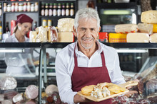 Smiling Salesman Holding Various Cheese On Board In Store