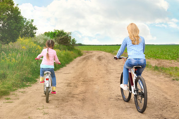 Poster - Mother with daughter riding bikes on country road