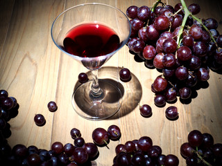 glass of wine and grapes on wooden table (dark light)