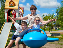 Child And Woman Fly On Blue Plane Attraction In City Park, Happy Family, Summer Vacation Concept