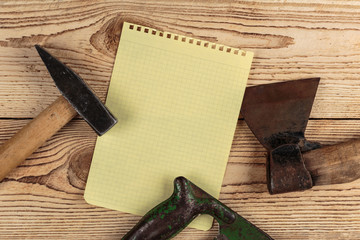 Old carpentry tools and a piece of notebook on a wooden backgrou