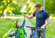 © Ermolaev Alexandr - father and son give high five while cycling in the park