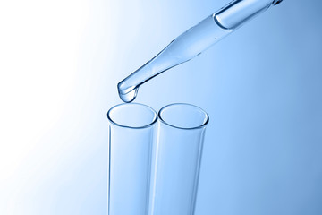 Wall Mural - Close up of a pipette dropping a  sample into a test tube on blue background