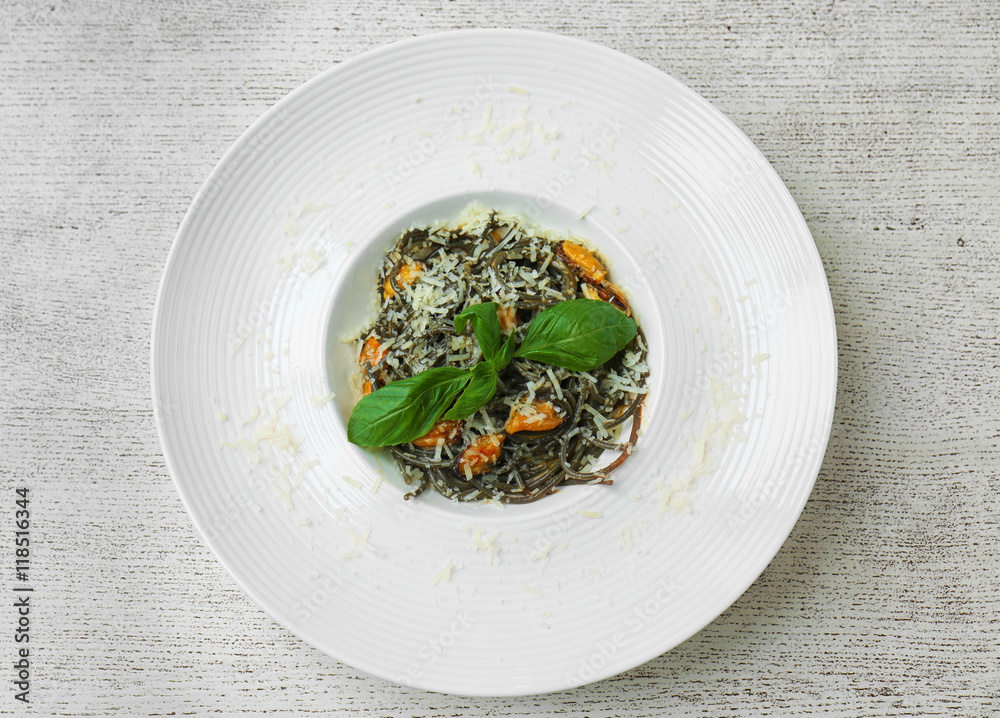Plate with black spaghetti, mussels and cheese on white wooden table