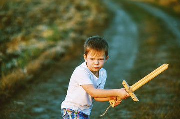 a boy plays with a wooden sword , on a dirt road .