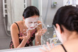 © kolotype - Woman with cosmetic mask spraying water on her face standing in