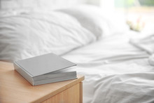 Closed book on wooden bedside table near crumpled bed