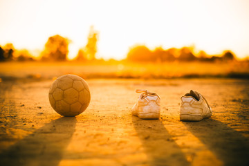 Wall Mural - an old ball with the shoes for street soccer football under the sunset ray light.